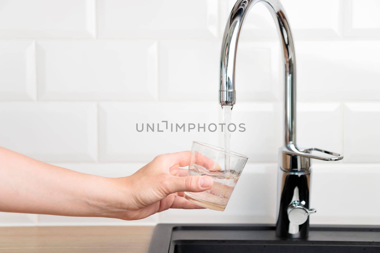Thirst human wanted to drink water and filling up a glass of tap pure water from kitchen faucet with white tiles wall. Concept of purity and cleanness of natural water with copy space