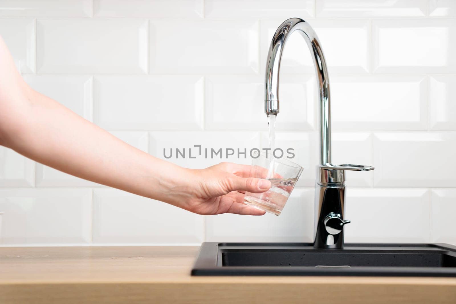 Thirst human wanted to drink water and filling up a glass of tap pure water from kitchen faucet with white tiles wall. Concept of purity and cleanness of natural water with copy space