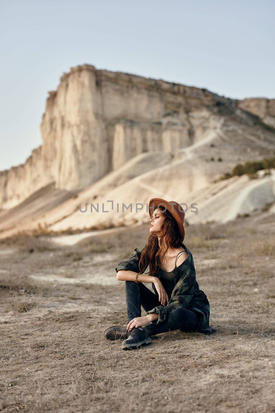 Woman wearing hat sits in front of mountain, admiring scenic view on sunny day by Vichizh