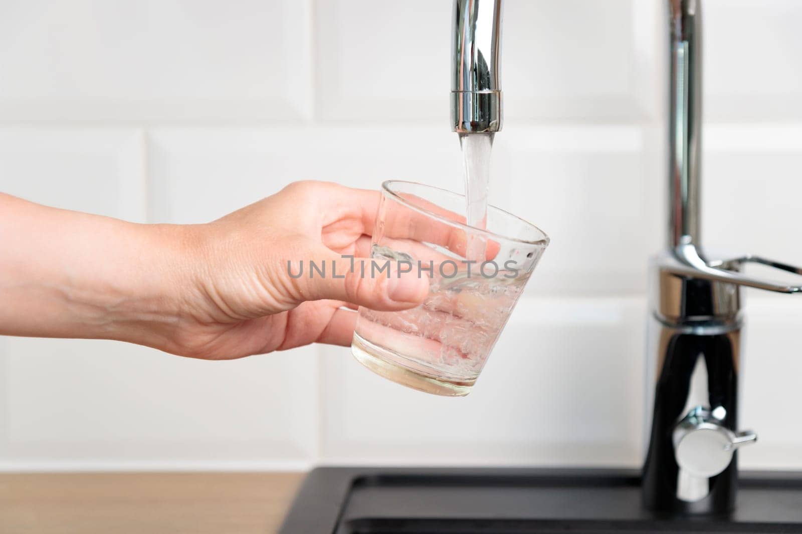 Thirst human wanted to drink water and filling up a glass of tap pure water from kitchen faucet with white tiles wall. Concept of purity and cleanness of natural water, banner with copy space