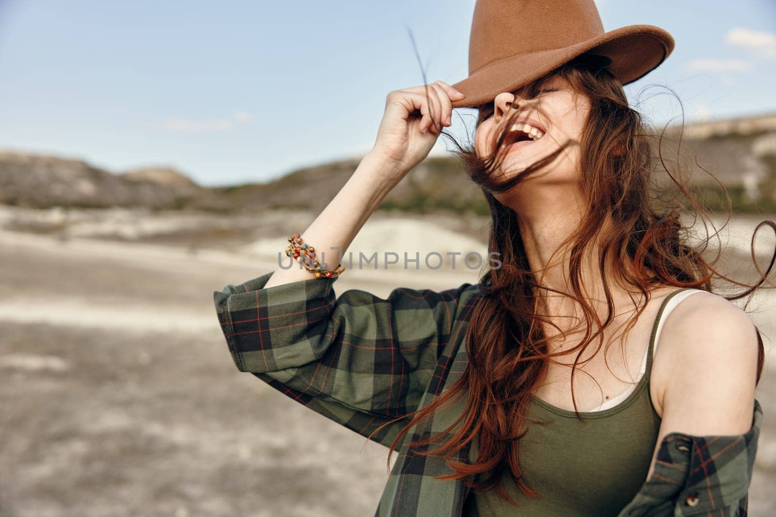 Happy woman in plaid shirt and brown hat smiling in sunny field by Vichizh