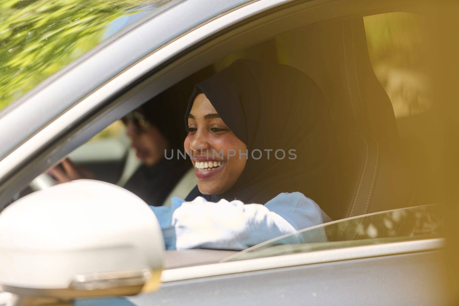 Two Muslim women wearing hijab converse on a smartphone while traveling together in a car through the.