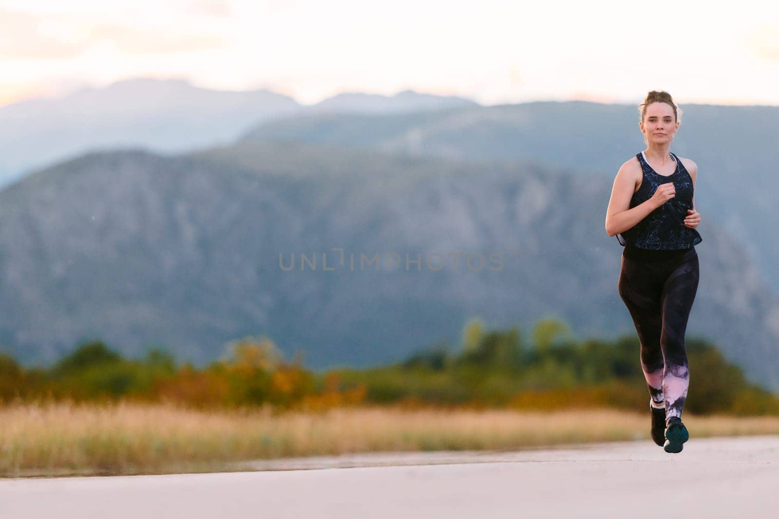 A determined athlete runs confidently under the sun, surrounded by stunning natural scenery, showcasing strength and resilience in her pursuit of fitness