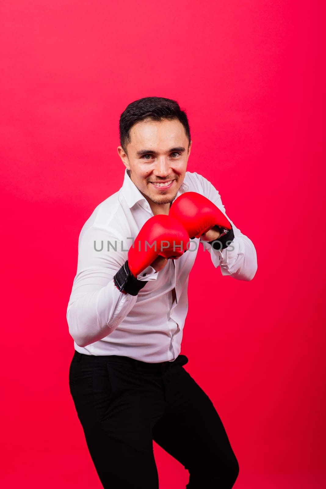 Handsome young businessman with boxing gloves. Studio red background by Zelenin