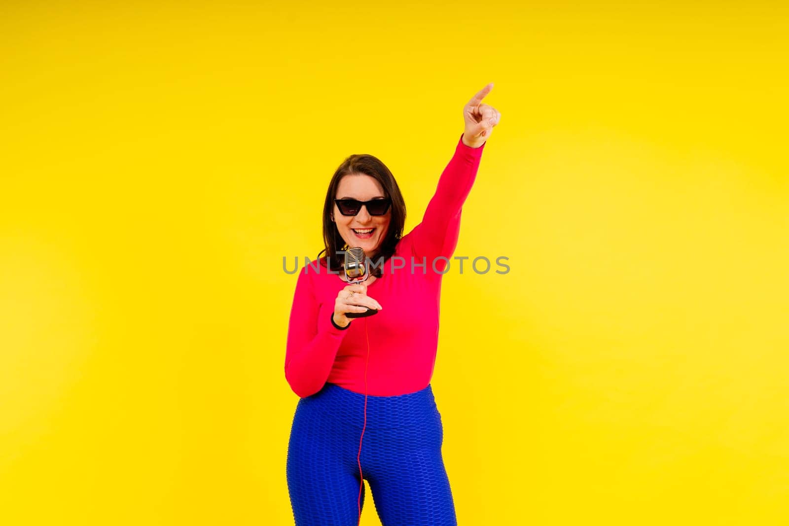 Smiling brunette woman with microphone on colored studio background by Zelenin