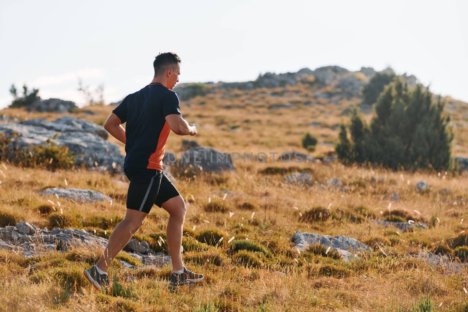 Determined Athlete Running Through Rugged Mountain Terrain at Sunrise. by dotshock