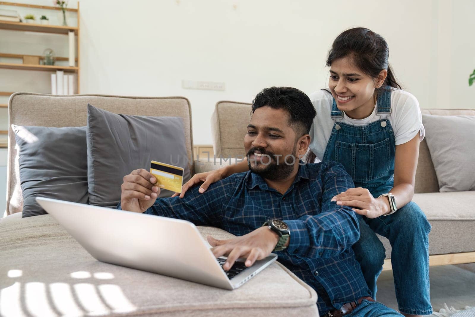 Indian couple using a laptop to pay bills and plan finances together in a cozy, modern living room setting.