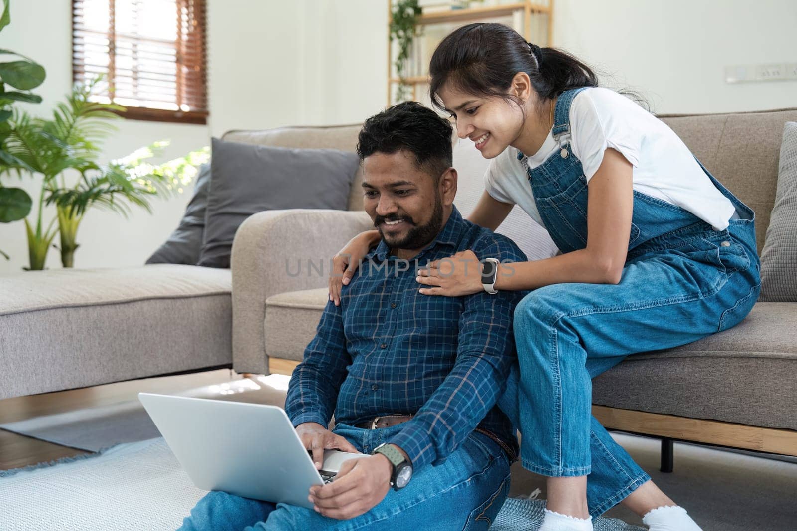 An Indian couple sitting in their living room, using a laptop to manage finances, pay bills, and plan their budget together. The scene captures a modern, everyday lifestyle.