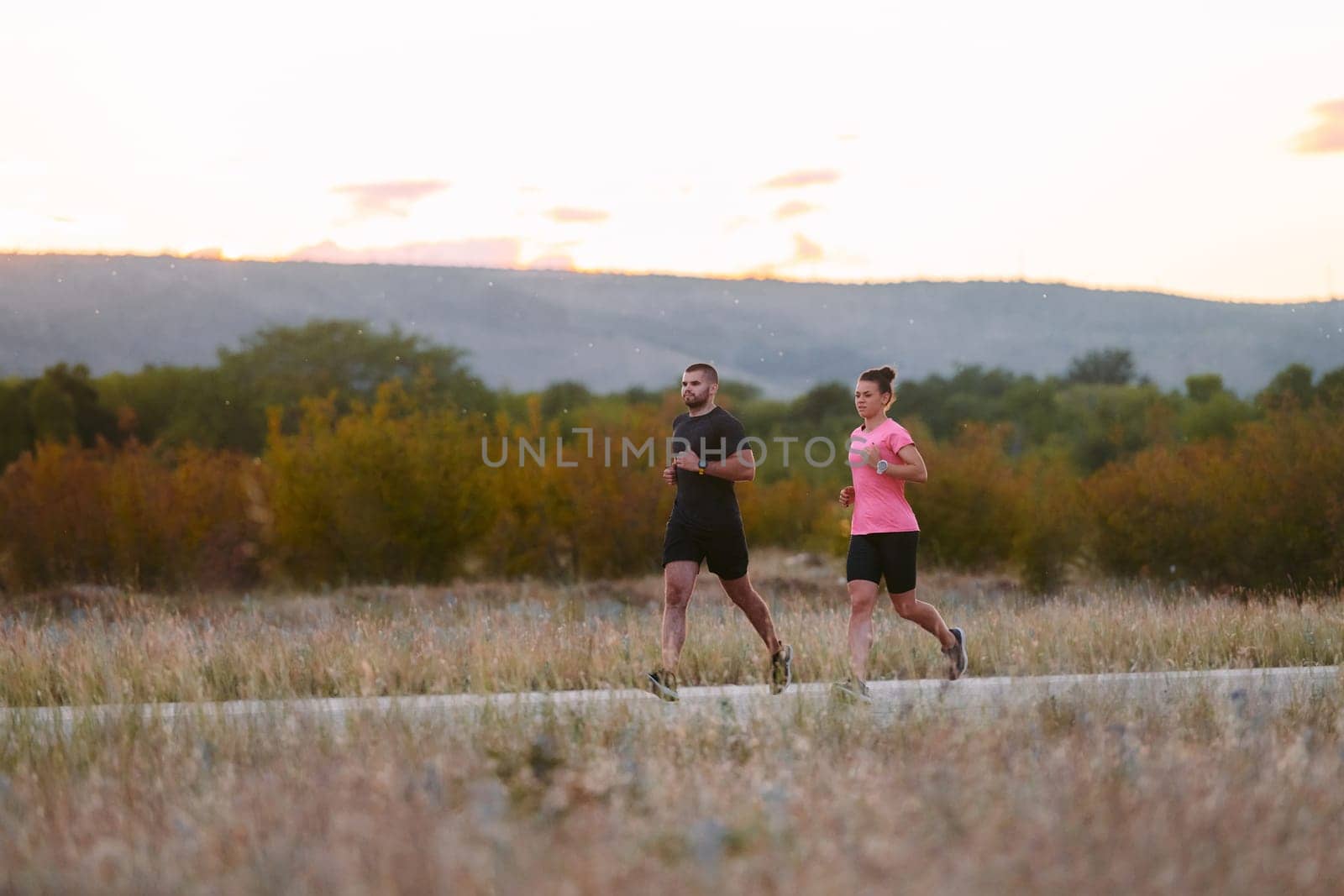 A couple dressed in sportswear runs along a scenic road during an early morning workout, enjoying the fresh air and maintaining a healthy lifestyle