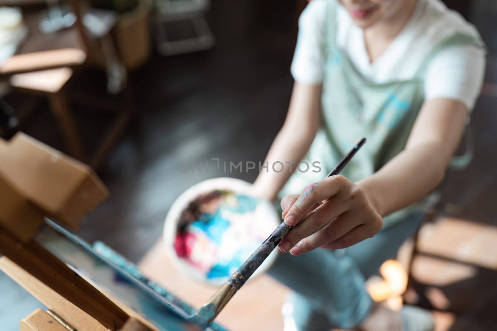 A person painting on a canvas with a brush and palette, showcasing the joy and creativity of engaging in a hobby in a home studio.