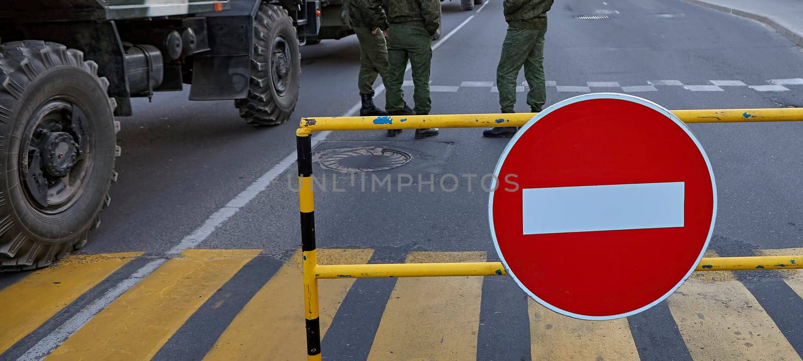 Armed soldiers at a roadblock with a no entry sign. Soldiers in full gear, carrying rifles. Roadblock made of metal barriers. No entry sign is large and red with a white border.