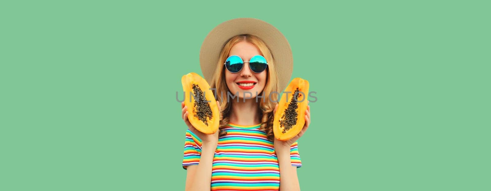 Summer portrait of happy cheerful young woman having fun with fresh papaya fruits wearing straw hat, sunglasses on green background, copy space