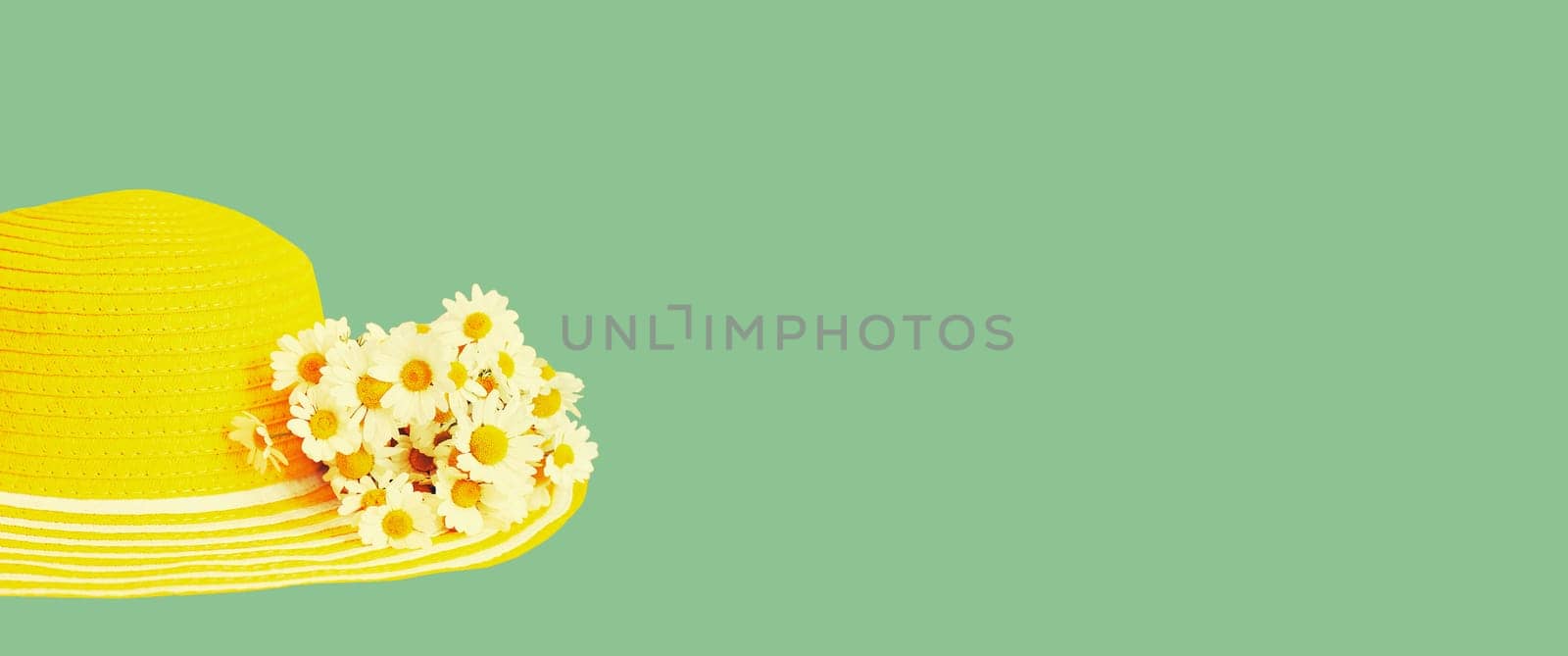 Summer yellow straw beach hat with chamomile flowers on green background, blank copy space for advertising text