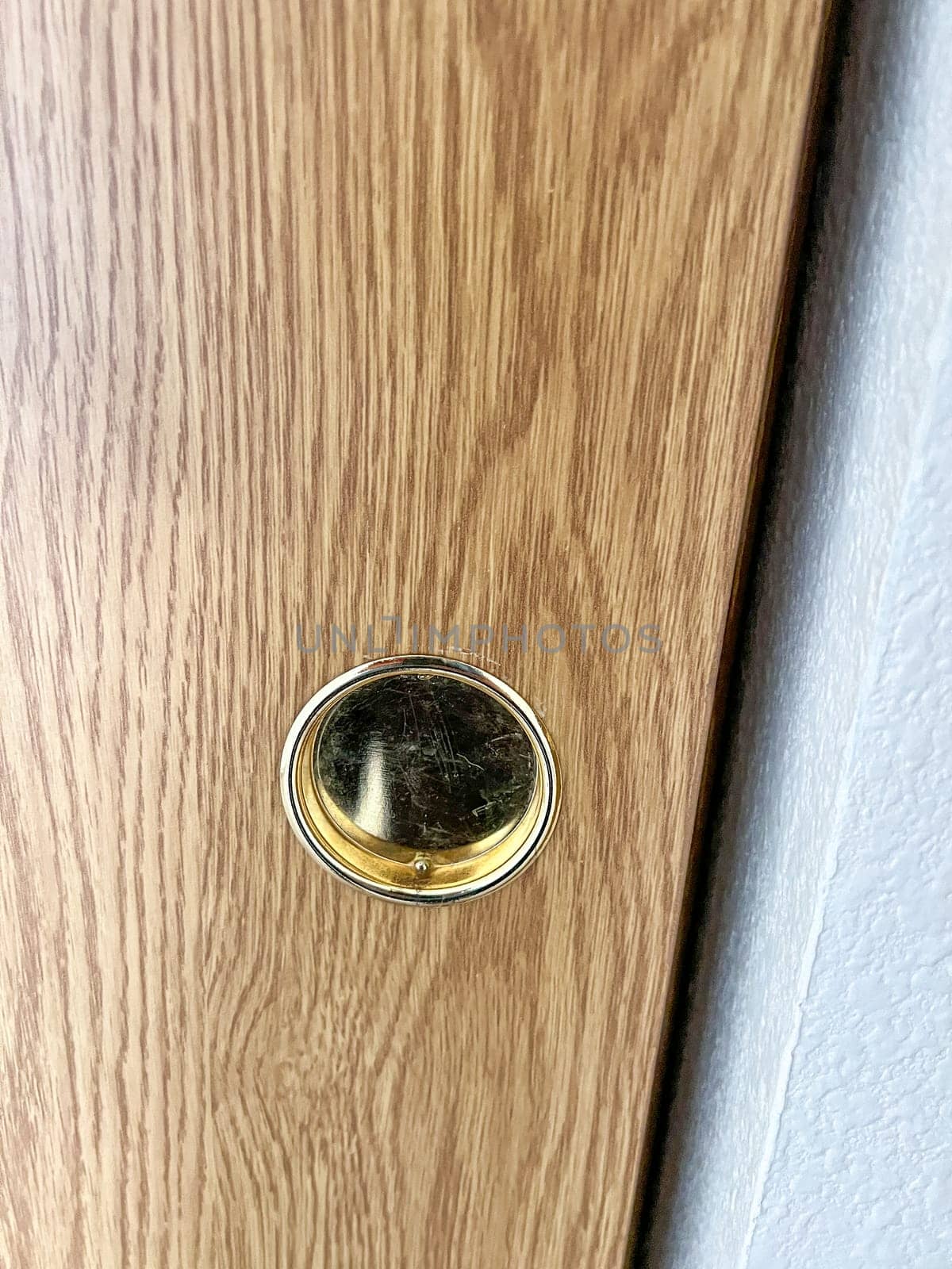 Detailed image of a brass door knob hole on a wooden closet sliding door, highlighting the grain and texture of the wood and the metallic sheen of the brass fitting.