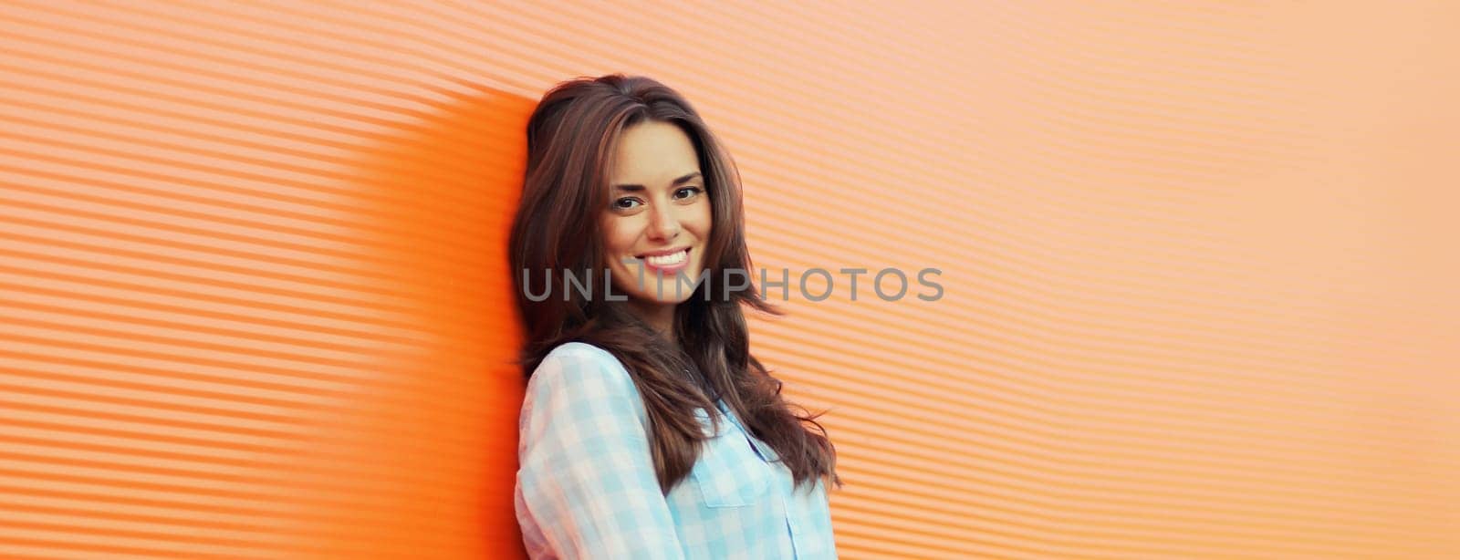 Portrait of beautiful happy smiling brunette young woman posing in the city on orange background