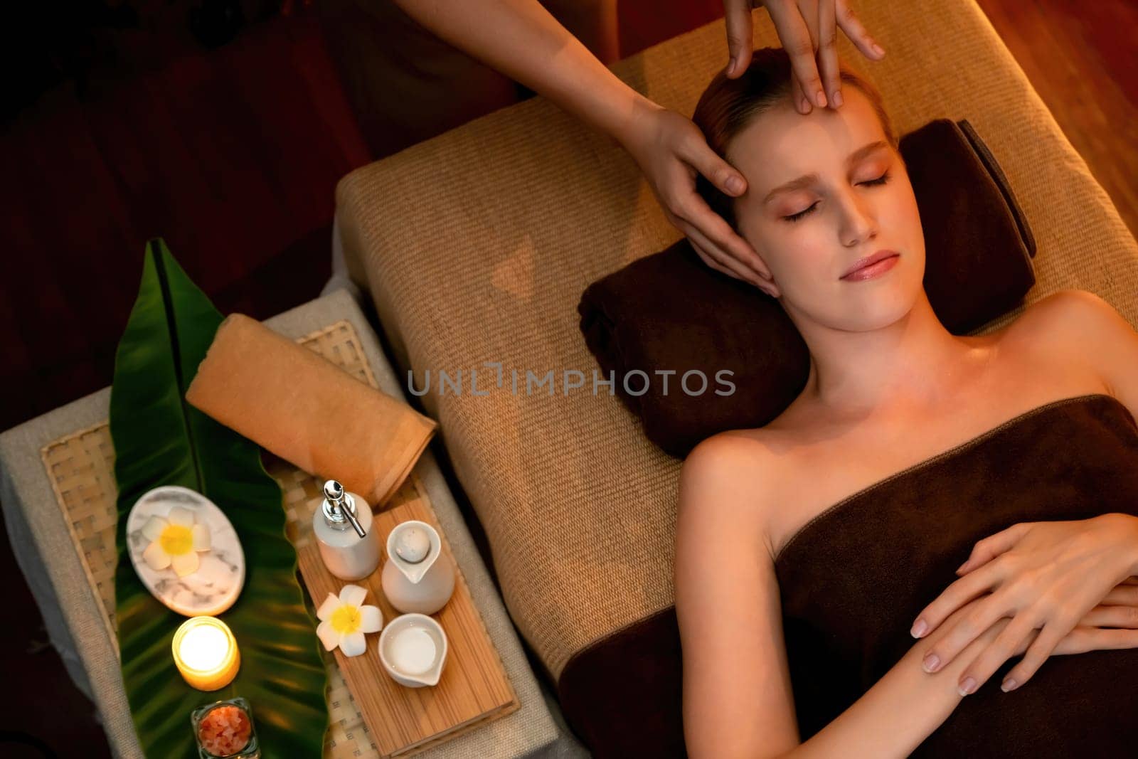 Caucasian woman enjoying relaxing anti-stress head massage and pampering facial beauty skin recreation leisure in warm candle lighting ambient salon spa in luxury resort or hotel. Quiescent