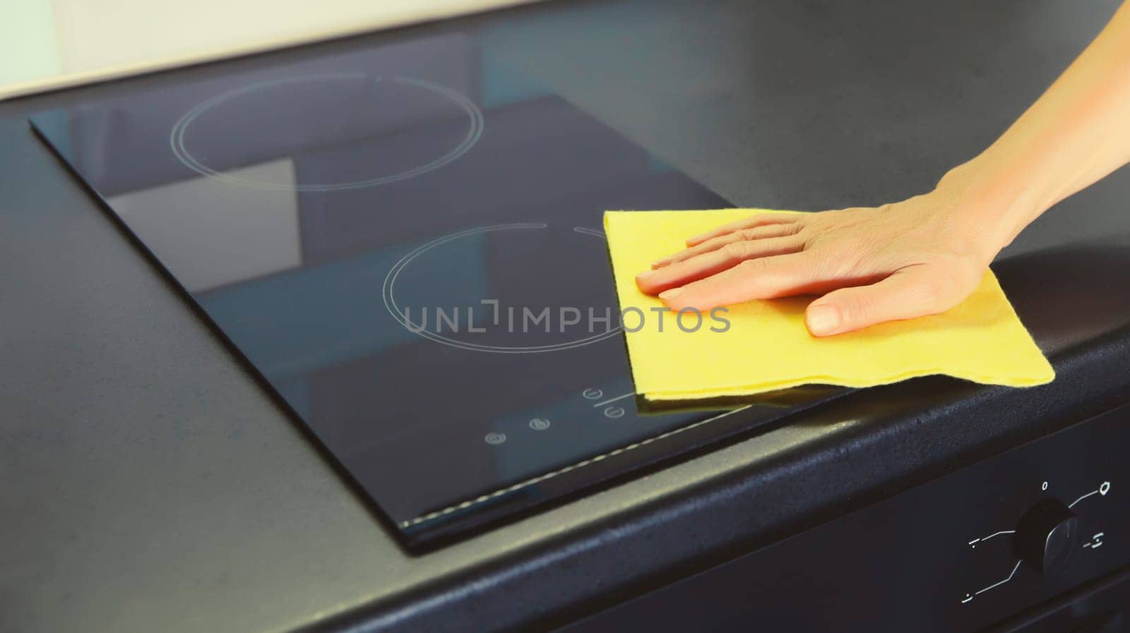House cleaning concept - woman holding dry microfiber rag wiping the glass surface induction cooker and kitchen countertop from dust