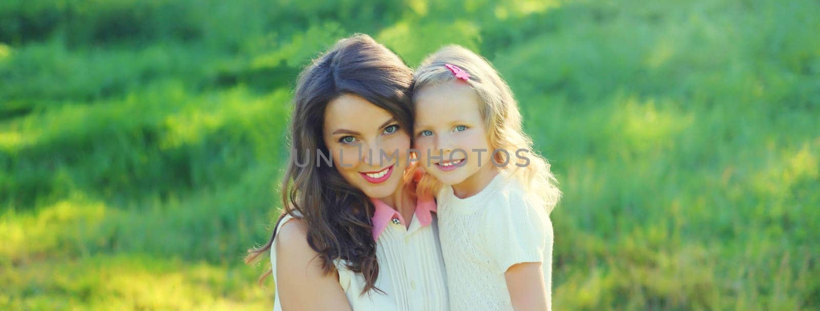 Portrait of happy cheerful smiling mother with little girl child daughter on the grass in sunny summer park