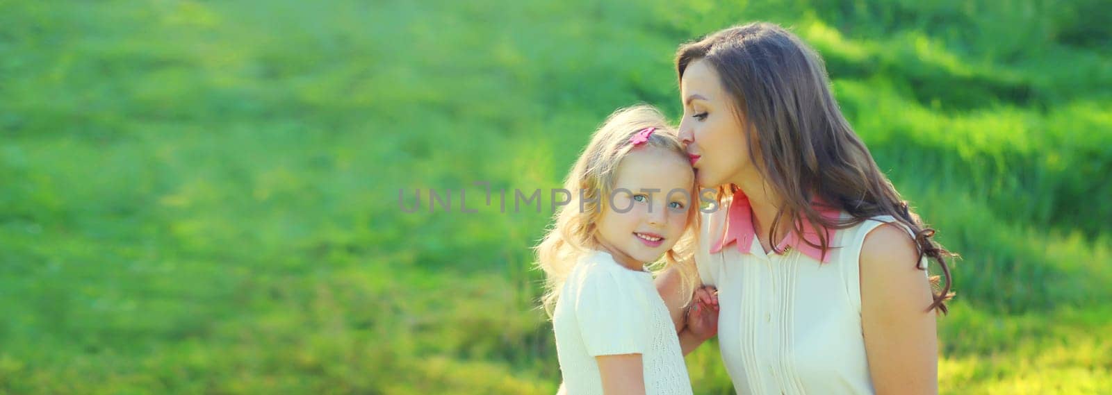 Happy cheerful smiling mother with little girl child daughter on the grass in sunny summer park by Rohappy