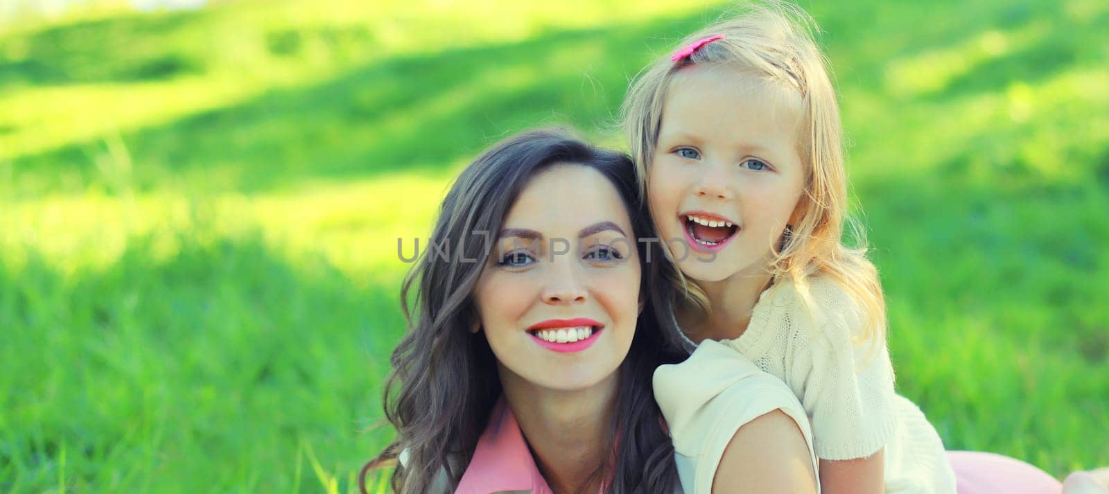 Happy cheerful smiling mother with little girl child daughter on the grass in sunny summer park by Rohappy