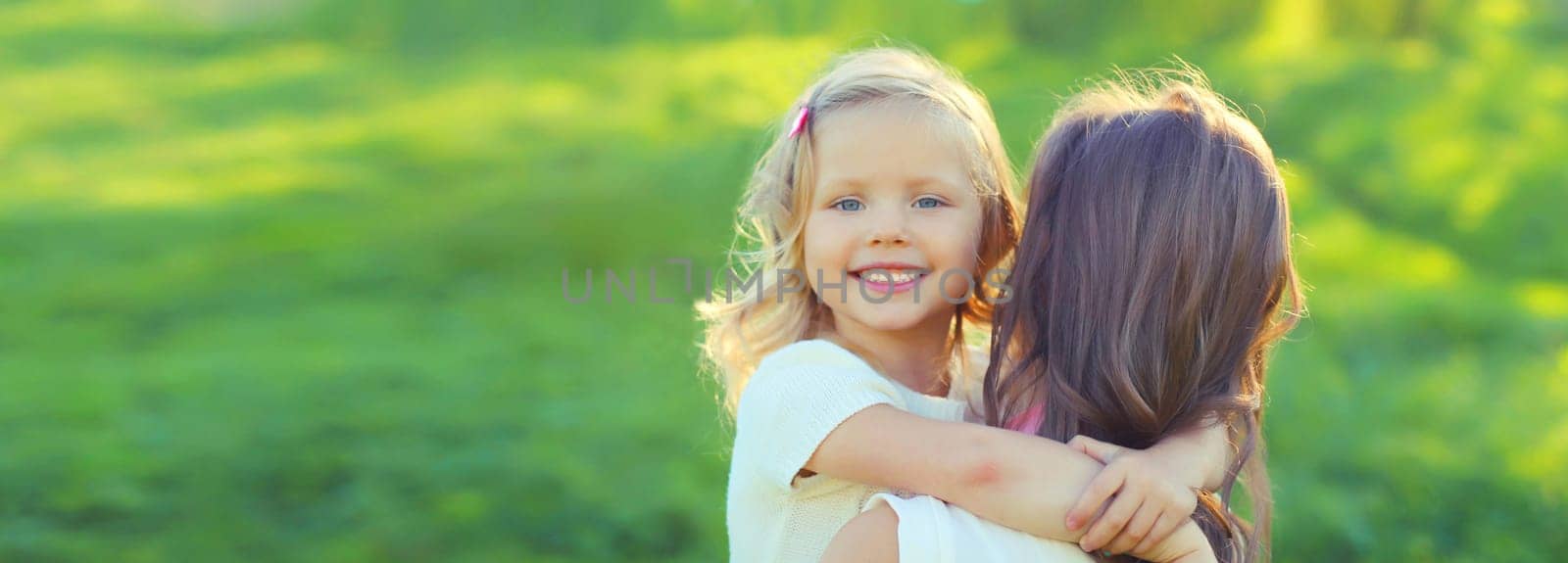 Happy cheerful smiling mother with little girl child daughter on the grass in sunny summer park by Rohappy