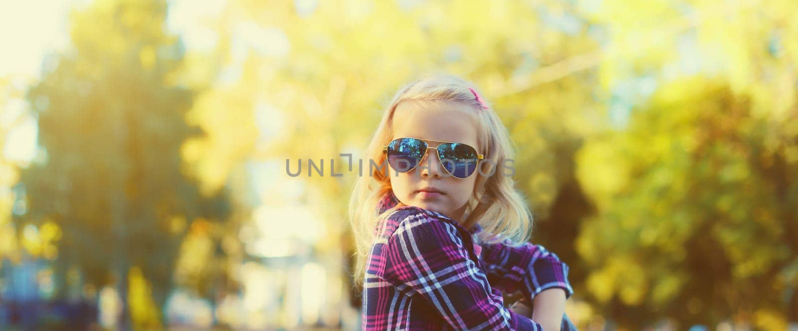 Stylish little kid girl posing in sunglasses looking away in sunny summer park