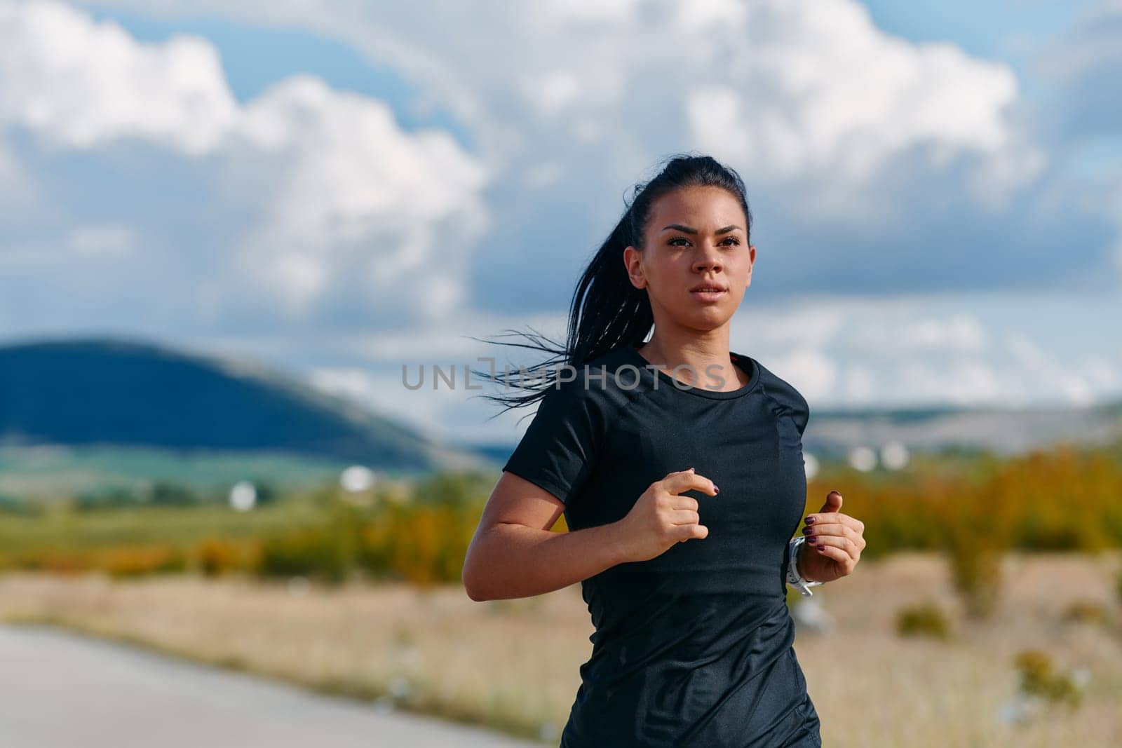 A determined athlete runs confidently under the sun, surrounded by stunning natural scenery, showcasing strength and resilience in her pursuit of fitness