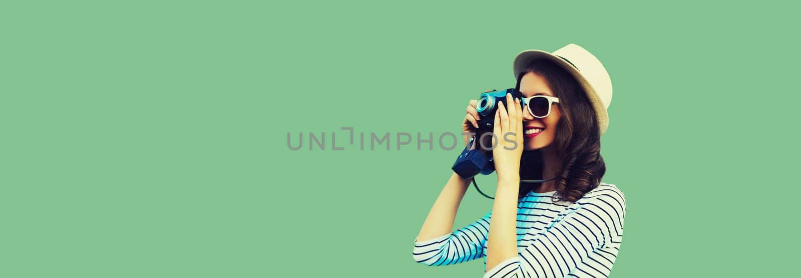 Summer portrait of happy smiling young woman photographer with film camera wearing summer straw hat on green background, blank copy space for advertising text