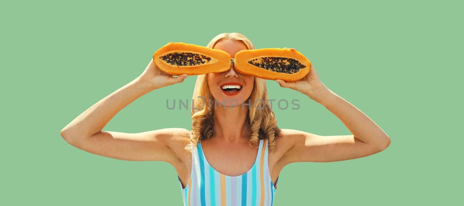 Summer portrait of happy cheerful laughing young woman posing with juicy papaya fruit on green background