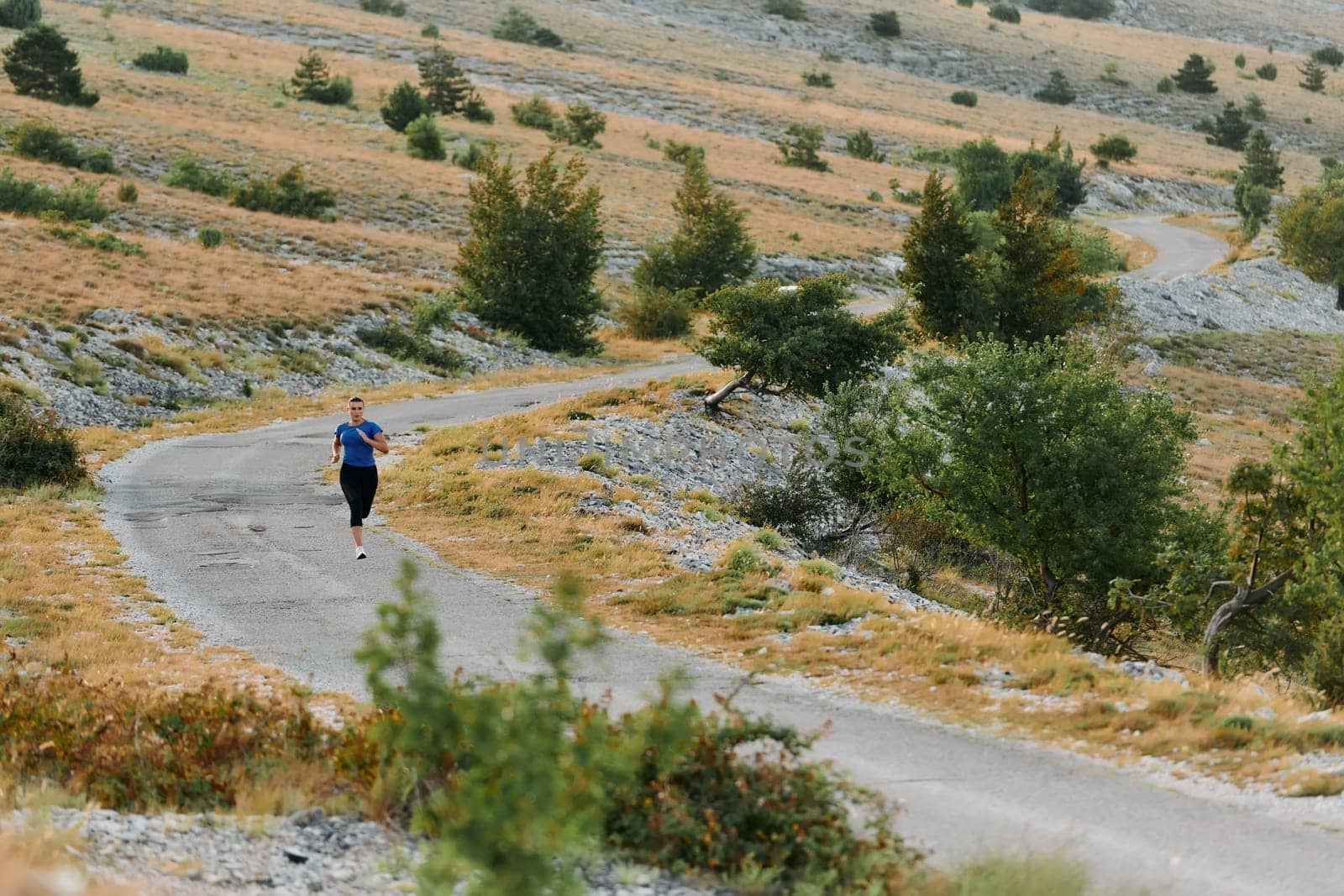 A determined female athlete runs through a forest trail at sunrise, surrounded by breathtaking natural beauty and vibrant greenery.