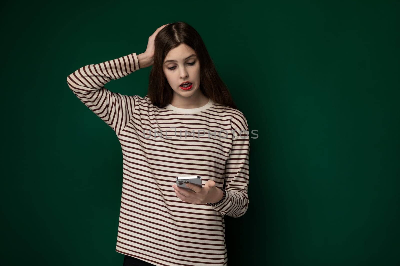 A woman wearing a striped shirt is standing, holding a cell phone in her hand.