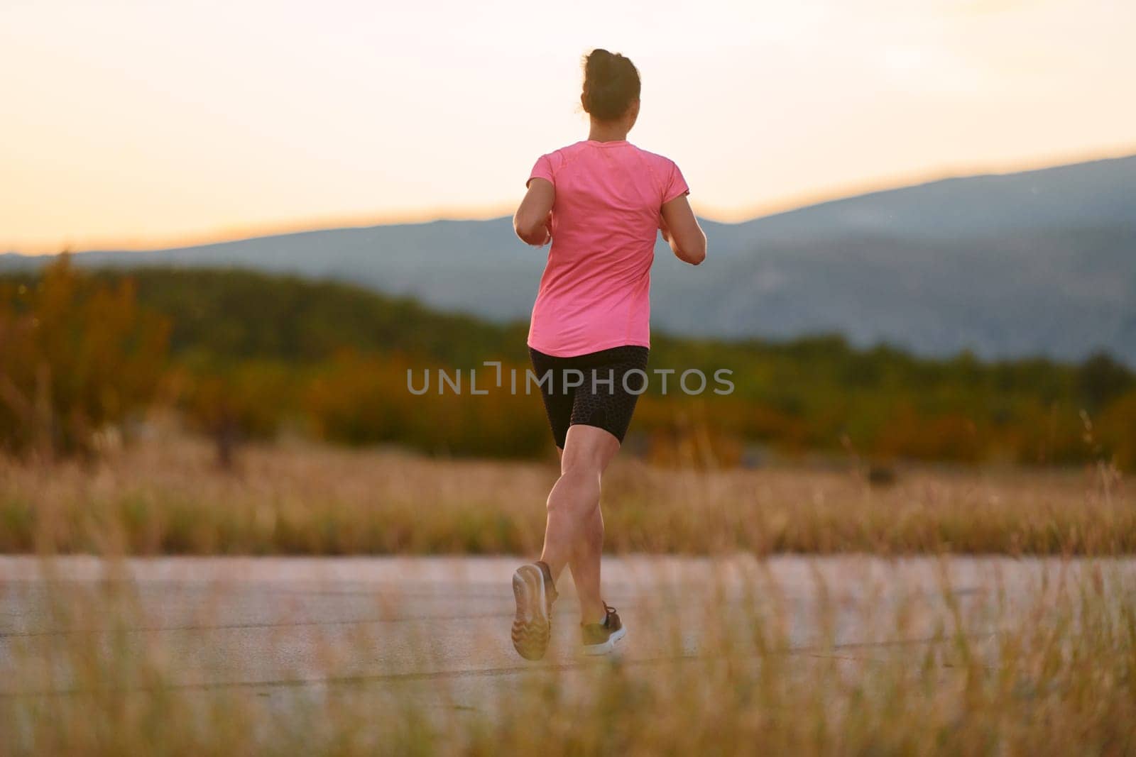 A determined athlete runs confidently under the sun, surrounded by stunning natural scenery, showcasing strength and resilience in her pursuit of fitness