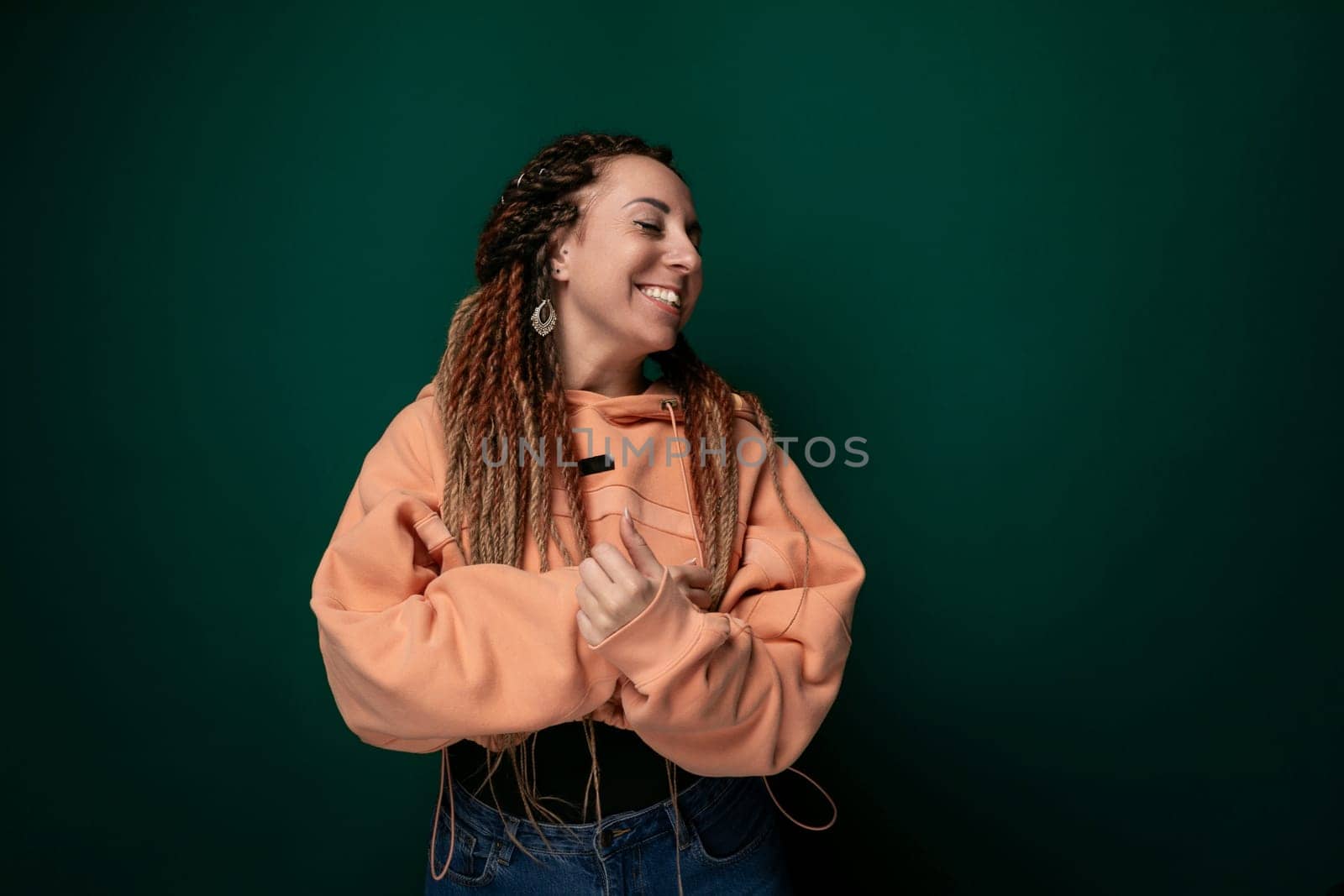 A woman with dreadlocks is standing in front of a solid green background. She appears confident and relaxed, with her hair styled in long, thick dreadlocks. The background adds a vibrant pop of color to the scene.