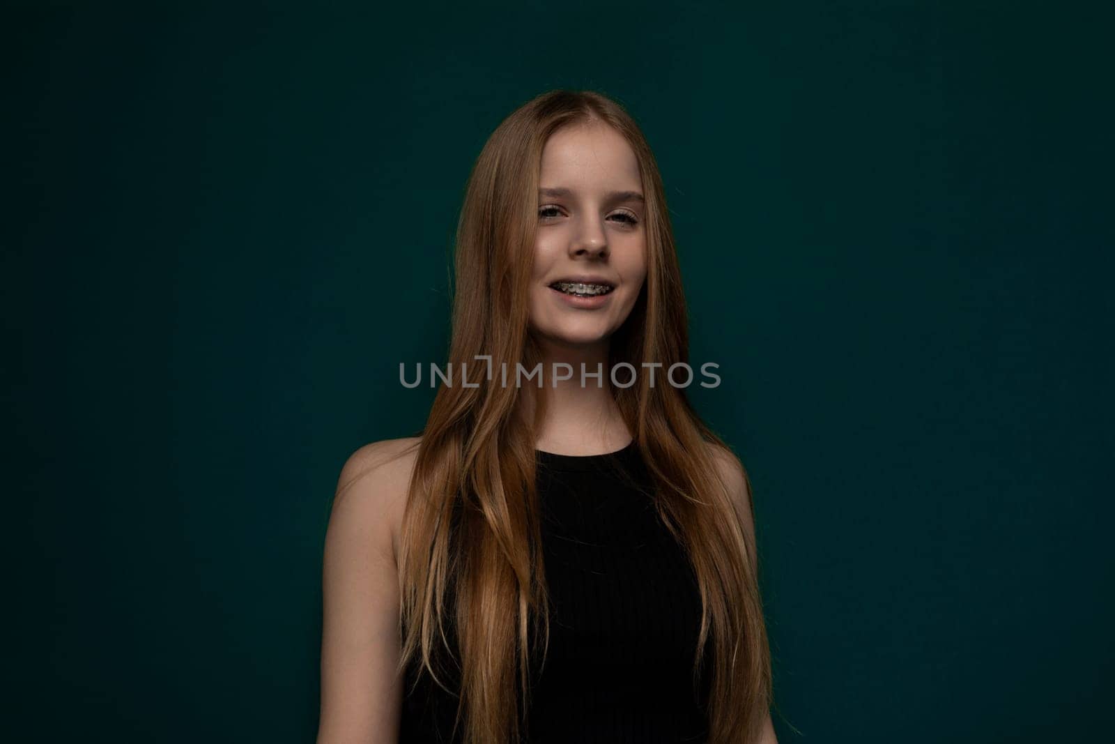 A woman with long red hair standing confidently in front of a vibrant green background. Her flowing hair contrasts beautifully with the verdant backdrop.