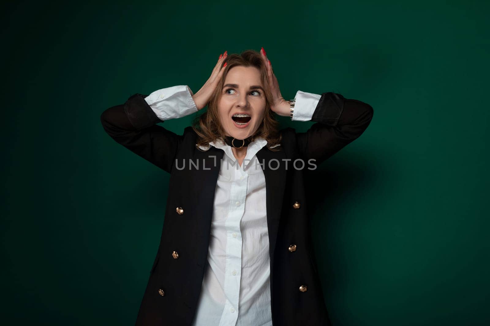 A woman standing while covering her ears with both hands, appearing to be shielding herself from loud or disturbing noise. She looks tense and uncomfortable as she seeks relief from the sound.