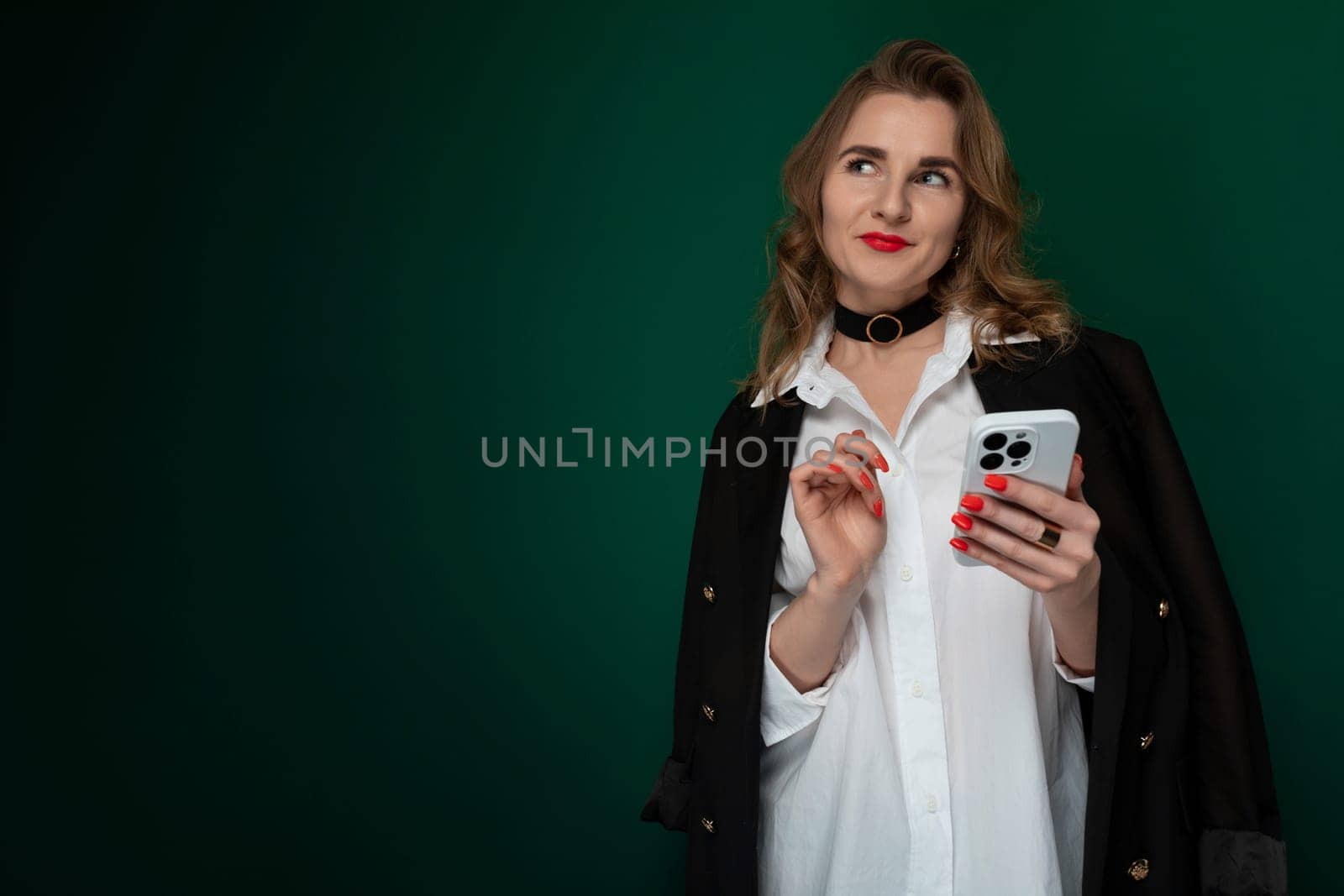 A woman wearing a white shirt is seen holding a cell phone in her hand, focusing on the screen intently. She appears engaged in a conversation or browsing content on the device.