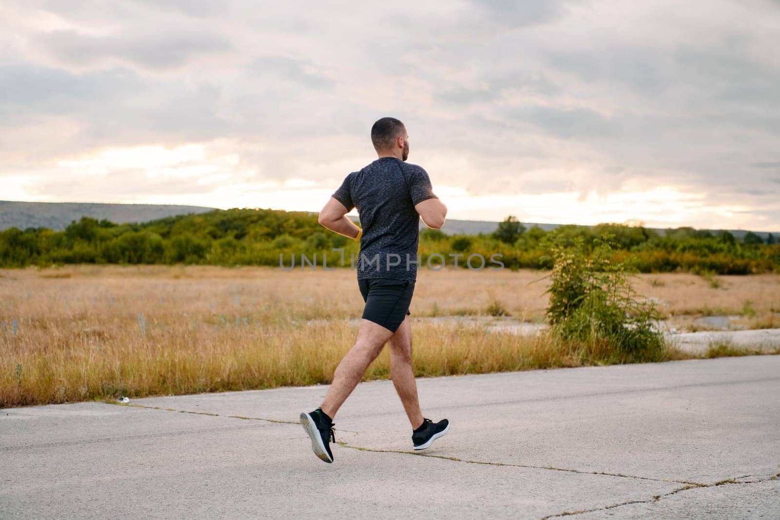 An athletic man jogs under the sun, conditioning his body for life's extreme challenges, exuding determination and strength in his preparation for the journey ahead