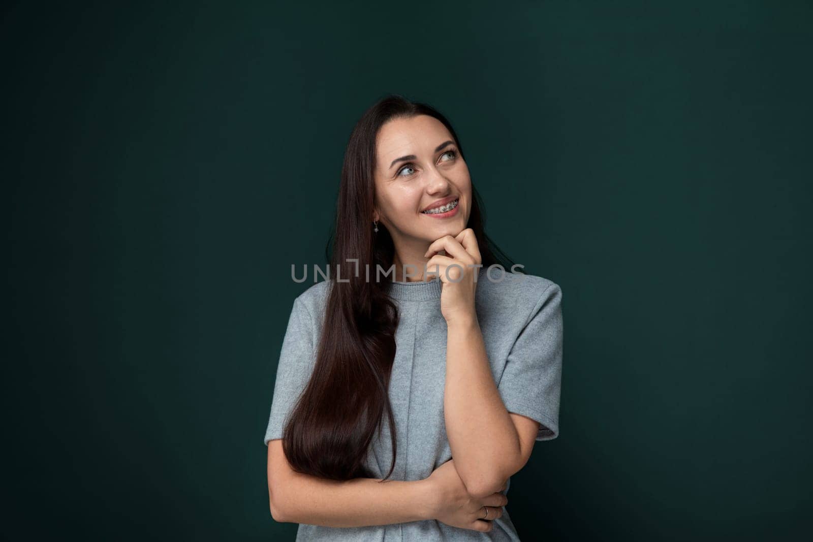 A woman is standing in front of a vibrant green wall. She is looking directly at the camera, with a neutral expression on her face. The background is plain, emphasizing the contrast between the woman and the wall.