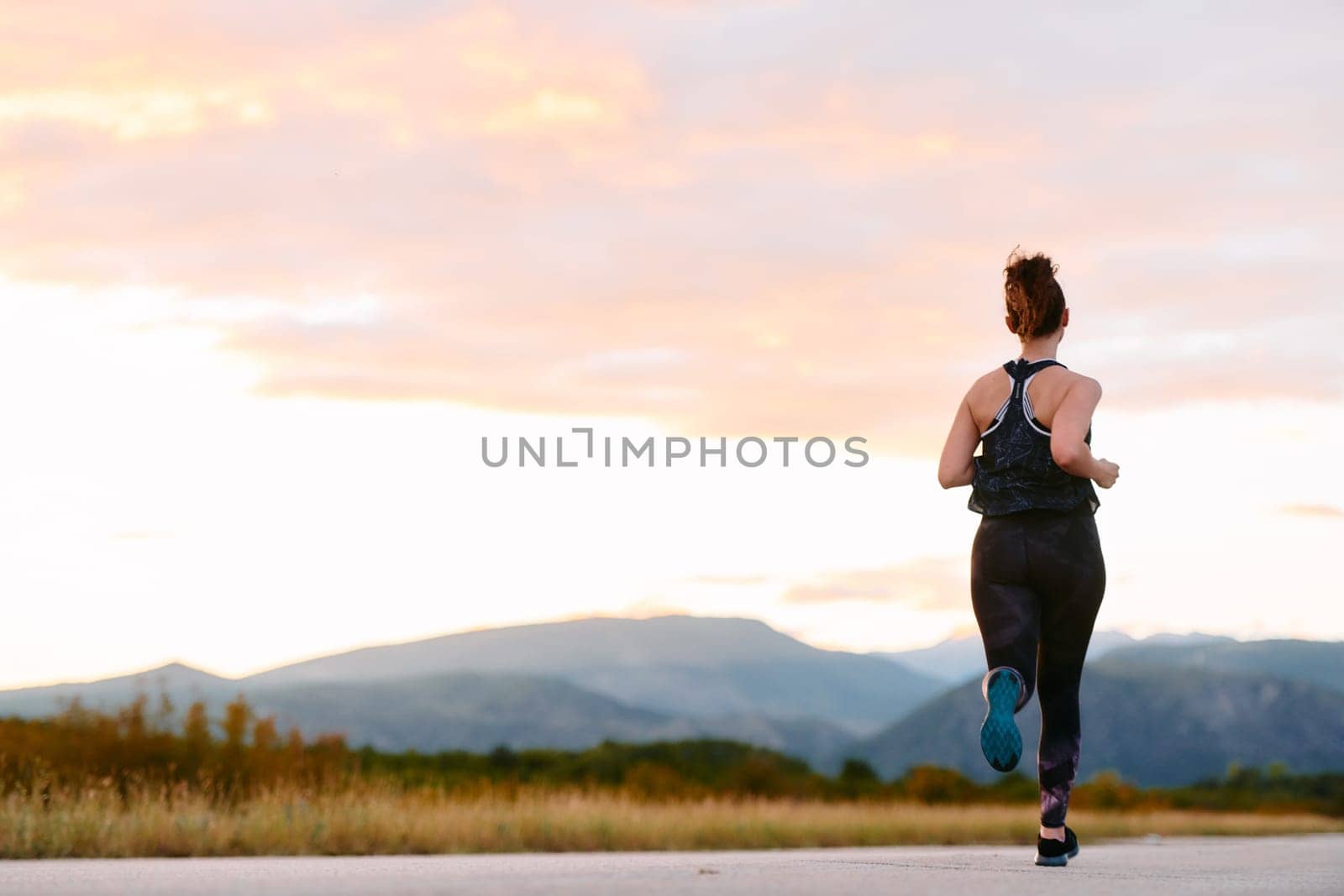 A determined athlete runs confidently under the sun, surrounded by stunning natural scenery, showcasing strength and resilience in her pursuit of fitness