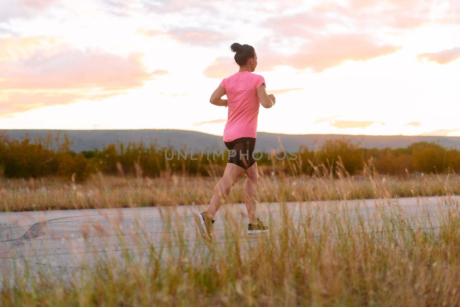 A determined athlete runs confidently under the sun, surrounded by stunning natural scenery, showcasing strength and resilience in her pursuit of fitness