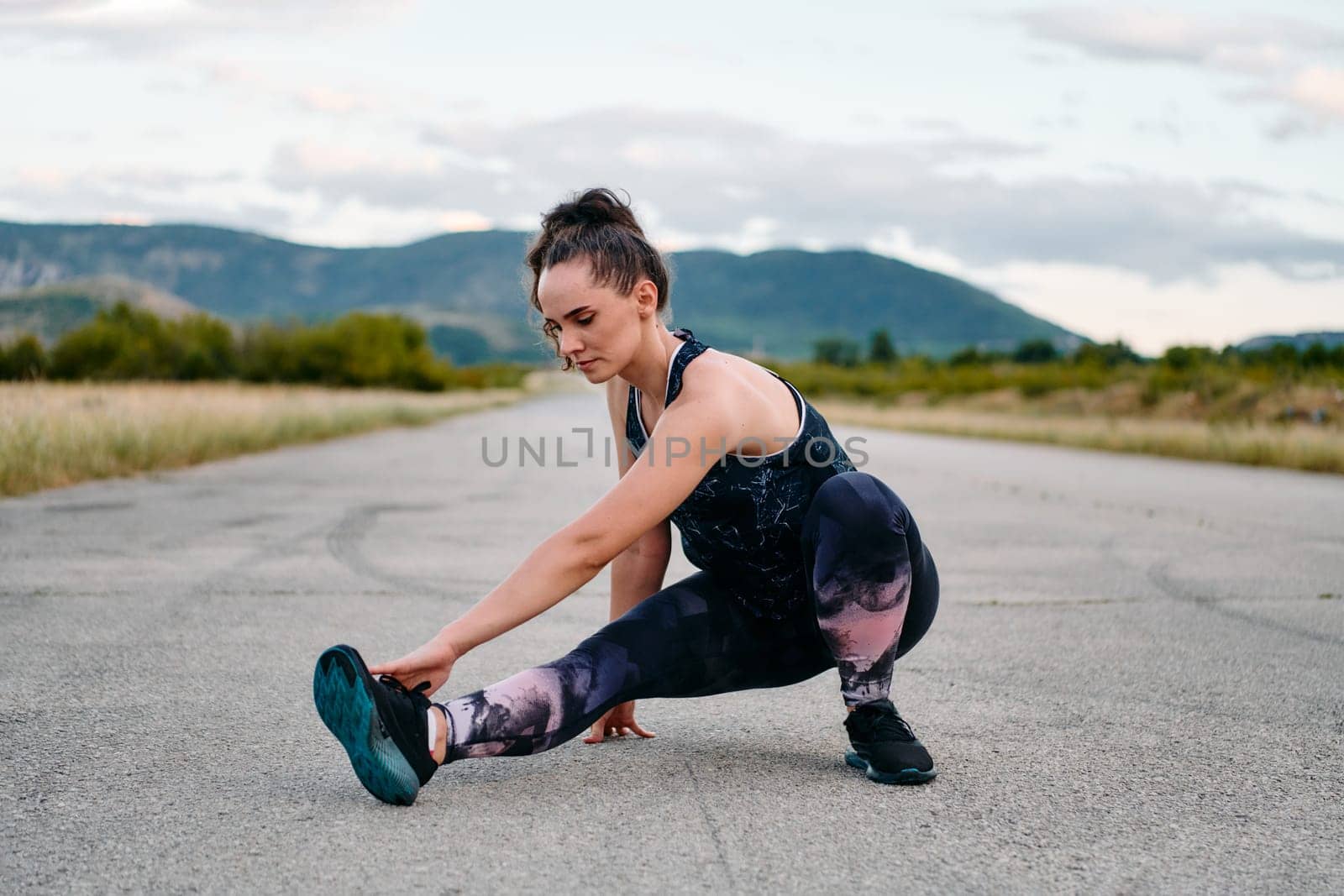 A determined female athlete stretches her muscles after a strenuous run through rugged mountain terrain, surrounded by breathtaking rocky landscapes.