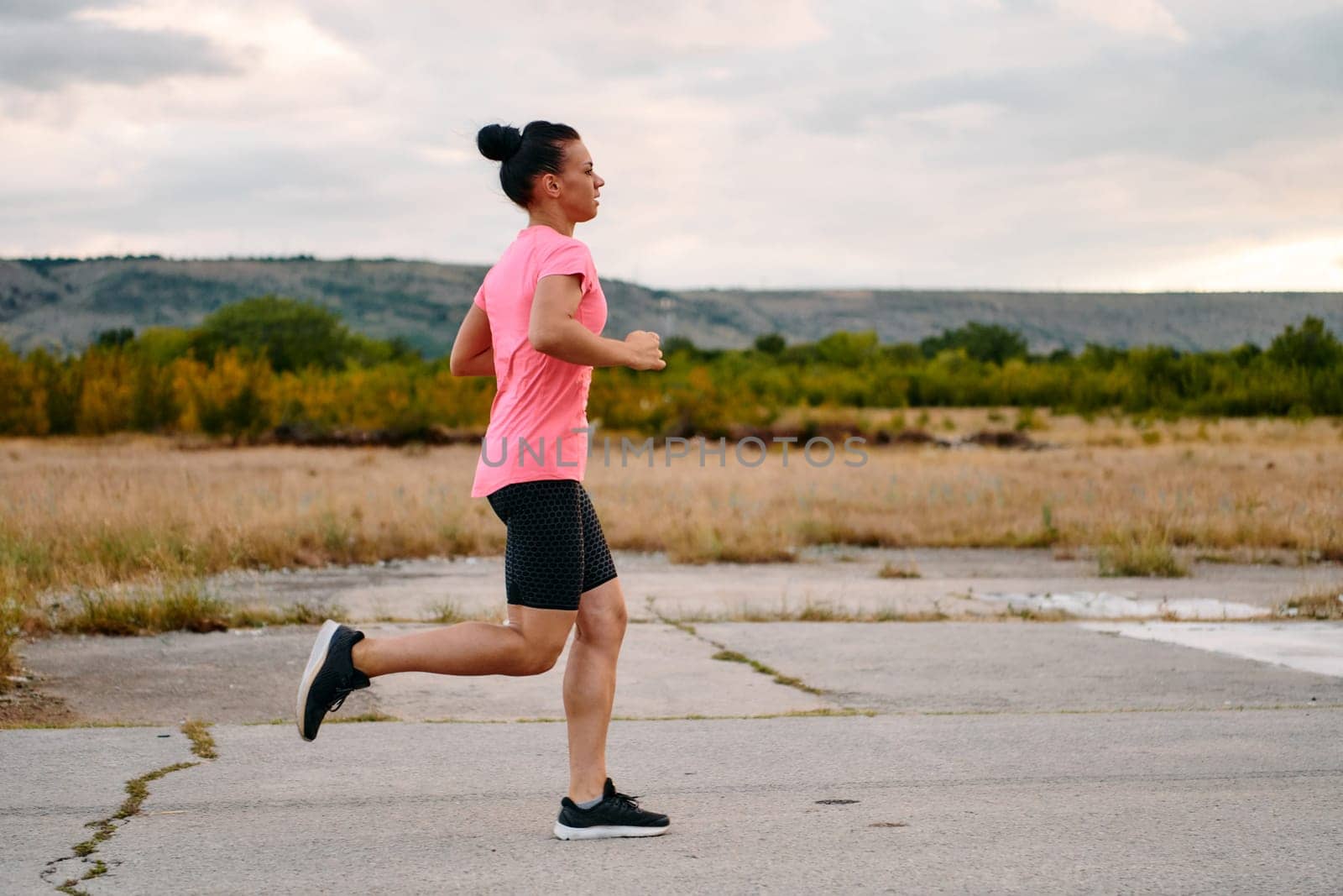 A determined athlete runs confidently under the sun, surrounded by stunning natural scenery, showcasing strength and resilience in her pursuit of fitness