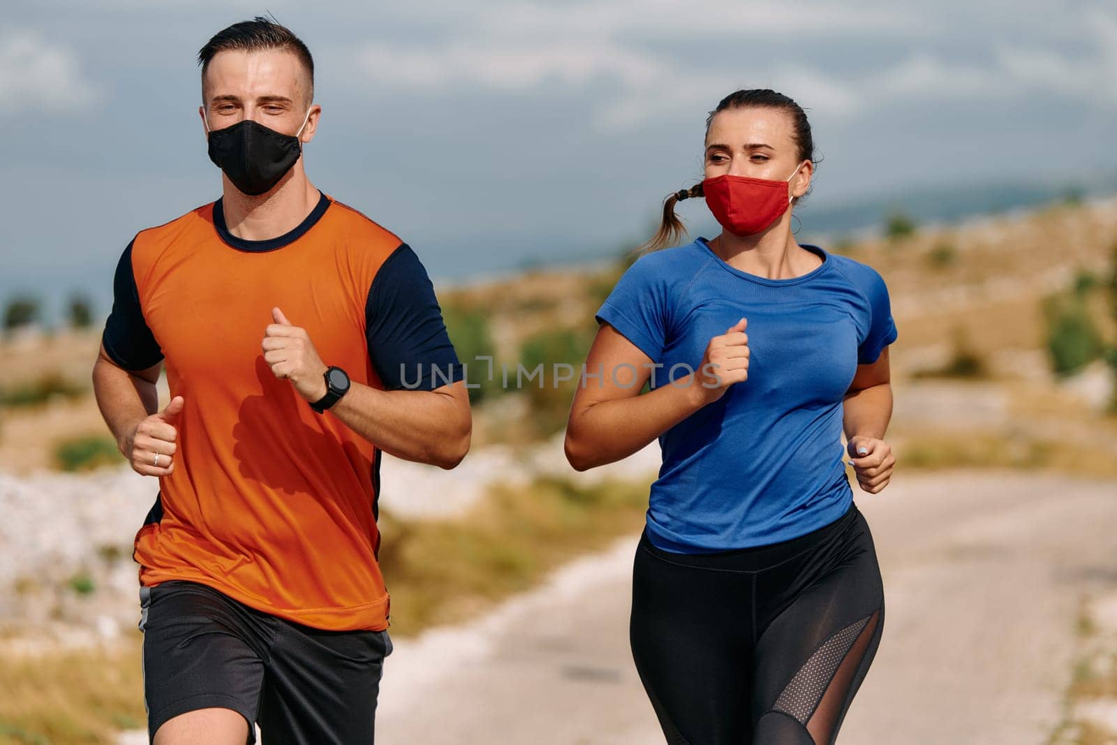 Couple running in nature at morning wearing protective face masks.