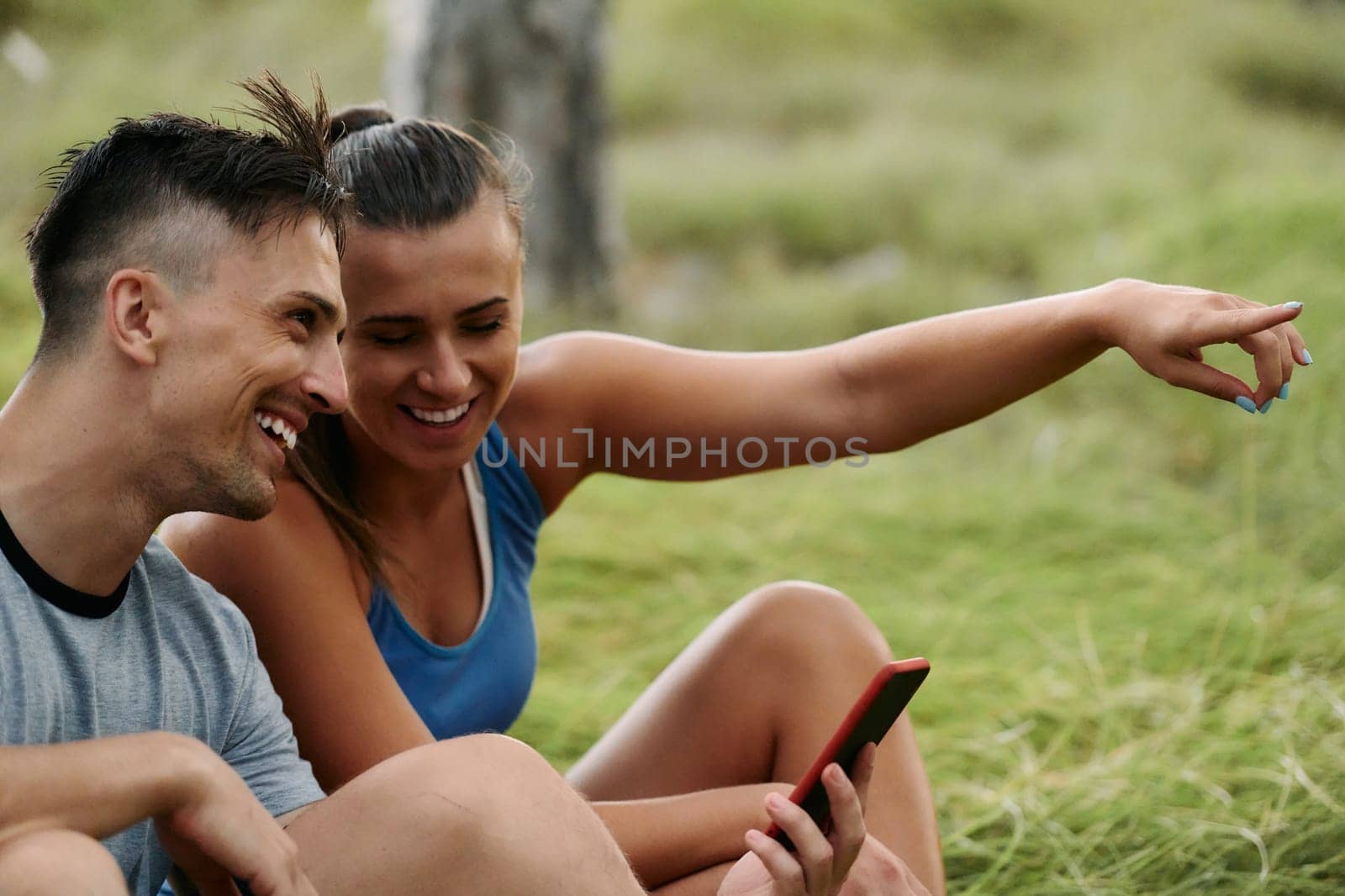 A romantic couple sits in the forest, browsing new running routes on their smartphone, embracing the beauty of nature as they plan their next outdoor adventure together