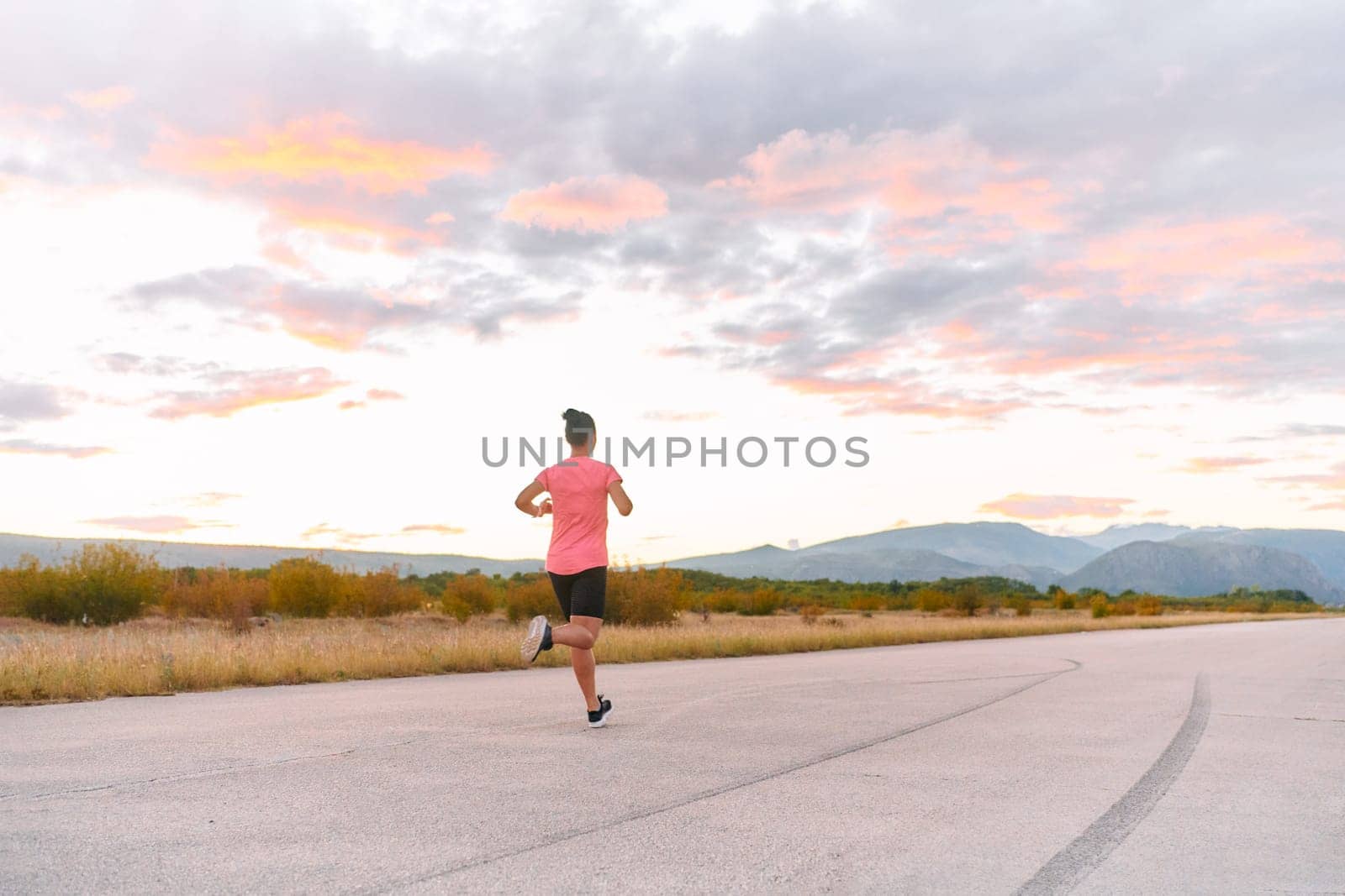 A determined athlete runs confidently under the sun, surrounded by stunning natural scenery, showcasing strength and resilience in her pursuit of fitness