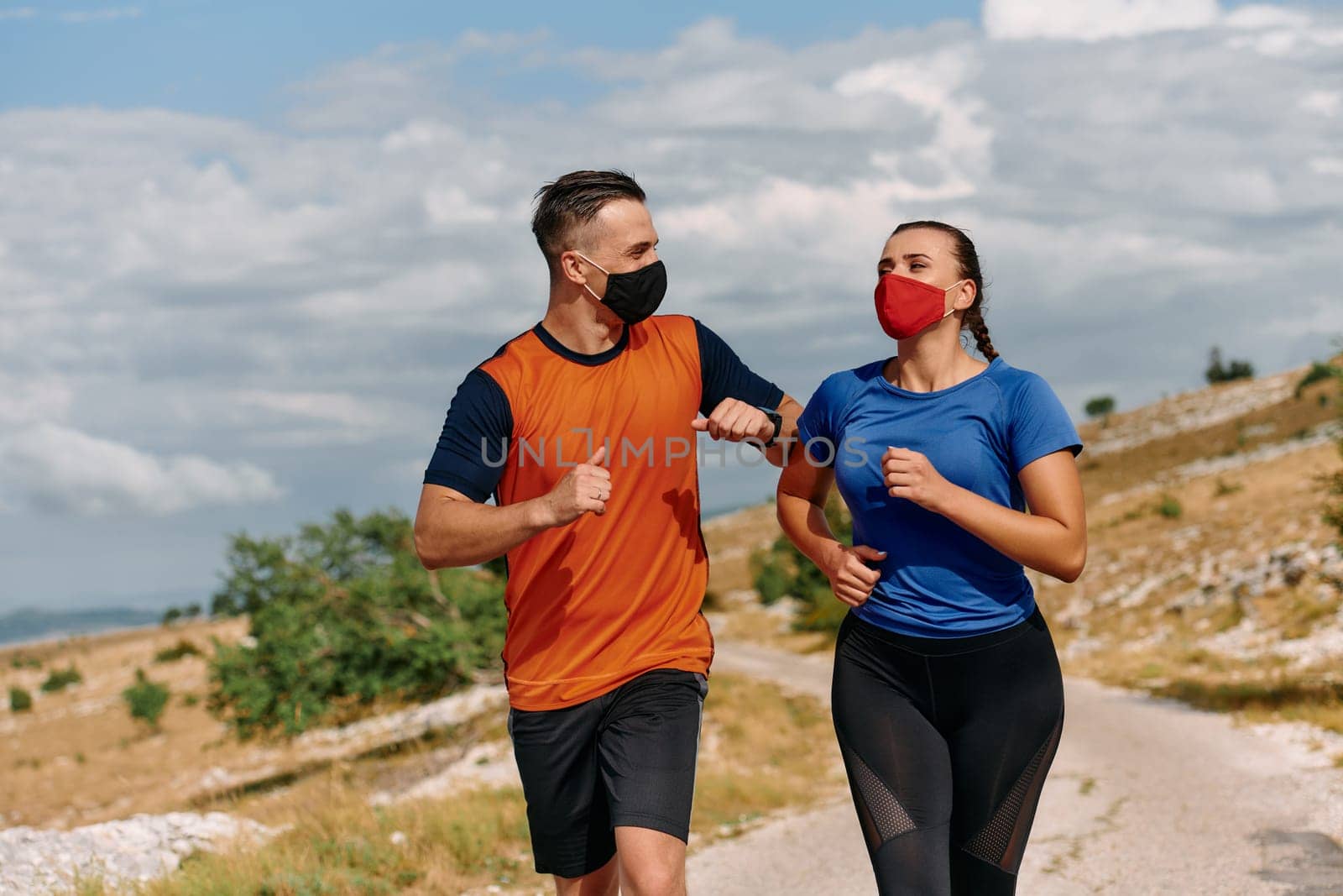 Couple running in nature at morning wearing protective face masks.