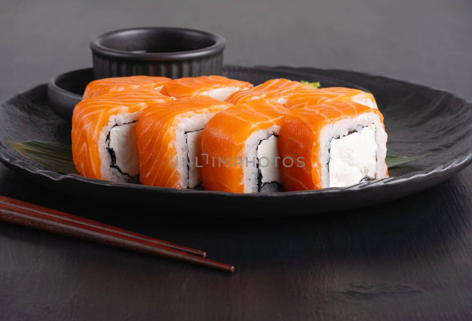 Philadelphia roll with salmon and cheese on plate on dark table.