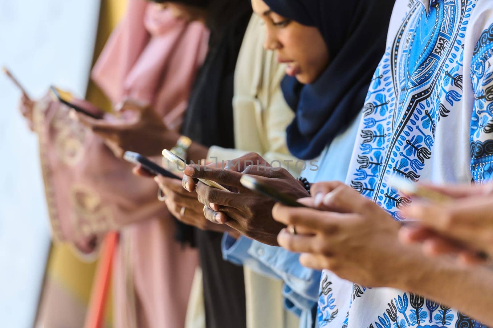 A diverse group of teenagers standing together against a wall, engrossed in their smartphones, showcasing modern connectivity and social interaction.