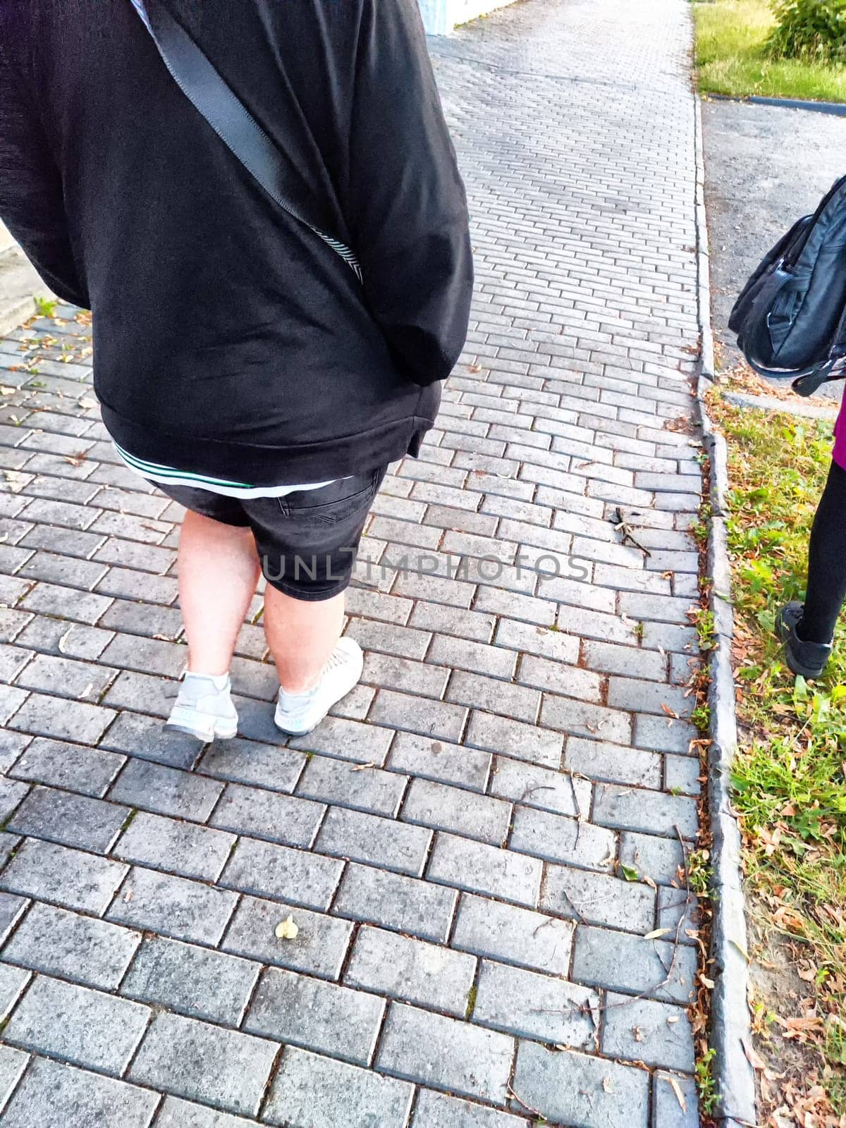 Person walking on a brick-laid path in the evening. Casual Stroll on Cobblestone Sidewalk at Dusk by keleny