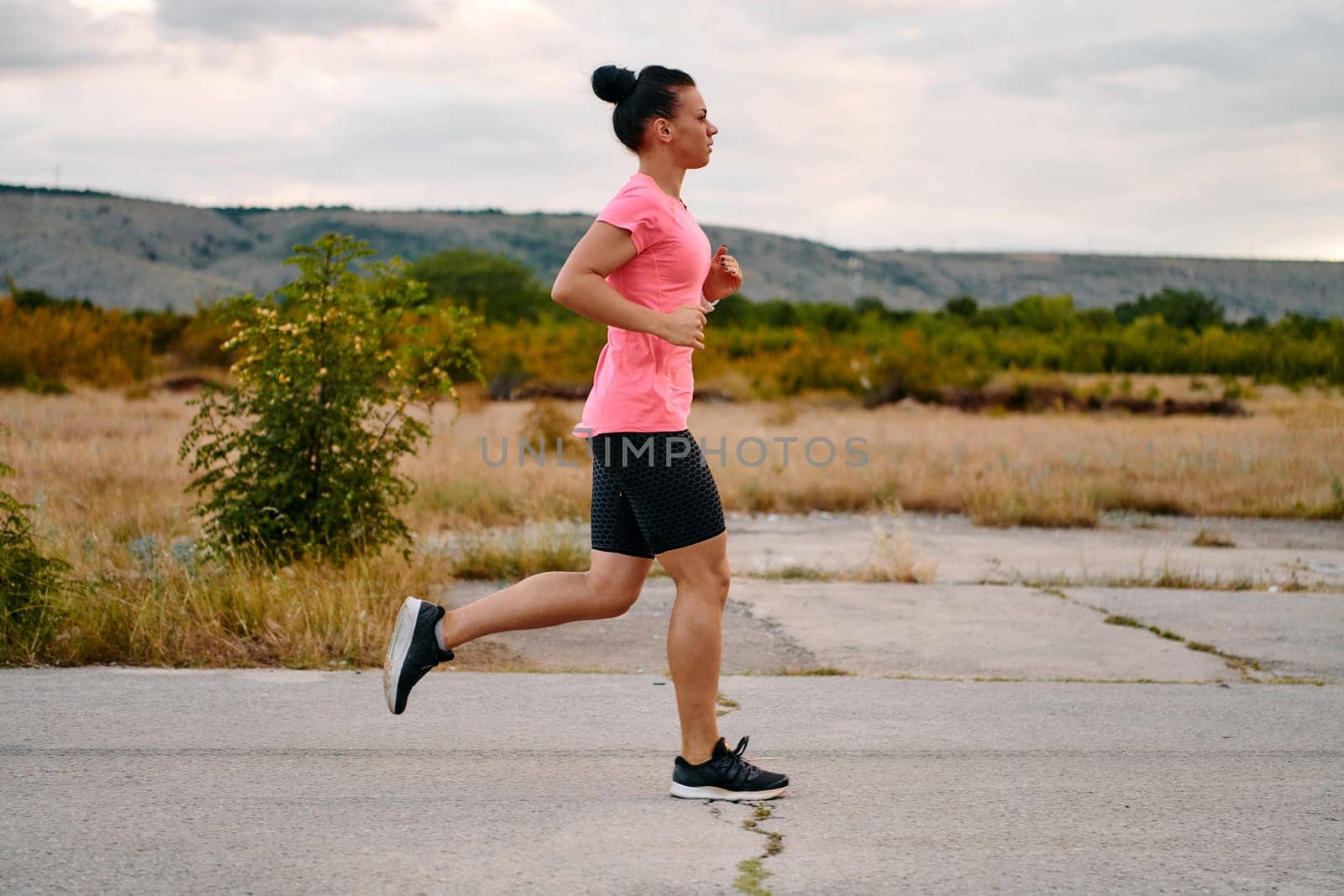 A determined athlete runs confidently under the sun, surrounded by stunning natural scenery, showcasing strength and resilience in her pursuit of fitness